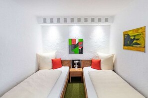 Ein Zimmer mit zwei Einzelbetten, einem kleinen Tisch und einem an der Wand hängenden Kunstwerk.