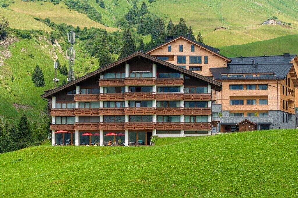 Un hôtel à plusieurs étages, doté d’une façade en bois, de balcons et offrant une vue sur une colline verdoyante.
