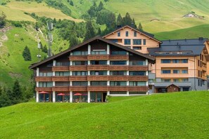 A multi-story hotel with a wooden facade, balconies, and a view of a green hillside. - Top 22 for 2-4 people/ 3rd floor (Schröcken)