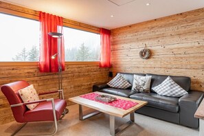 Une pièce avec un mur en bois, un canapé en cuir noir, une chaise rouge et une table avec un set de table.