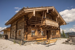 A rustic wooden chalet with a balcony, stone foundation, and a bench outside. - Vrbo Property (Saalbach)