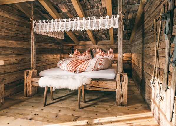 A rustic wooden cabin bedroom with a bed, pillows, and a fur throw. - Vrbo Property (Saalbach)