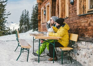 A wooden cabin with a bench and a table, surrounded by snow and trees. - Vrbo Property (Saalbach)