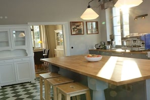 Eine Küche mit einer Holztheke, Barhocker, einer Kaffeemaschine und einem Fenster, das für natürliches Licht sorgt.