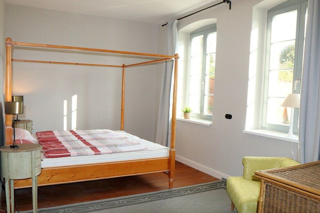 Un letto a baldacchino con struttura in legno, un comodino con lampada e una poltrona verde.