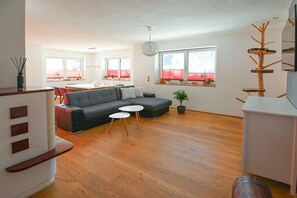 A modern living room with a sectional sofa, two small round tables, and a wooden floor. - Holiday home in Rauris with swimming pool (Rauris)