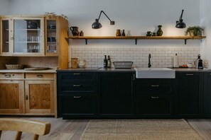 Una cocina con armarios oscuros, encimera de madera, pileta blanca y dos lámparas colgantes negras.