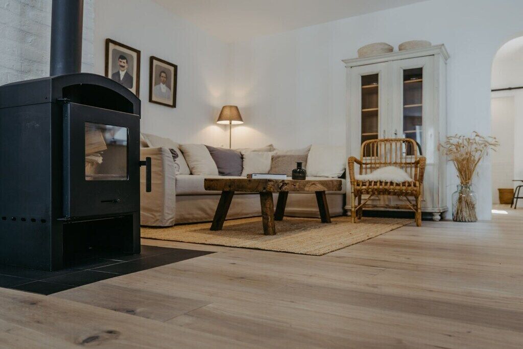 Ein Wohnzimmer mit einem schwarzen Kaminofen, einem Sofa, einem Holztisch, einem Korbstuhl und einem weißen Schrank mit Glastüren.