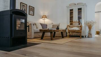 Ein Wohnzimmer mit einem schwarzen Kaminofen, einem Sofa, einem Holztisch, einem Korbstuhl und einem weißen Schrank mit Glastüren.