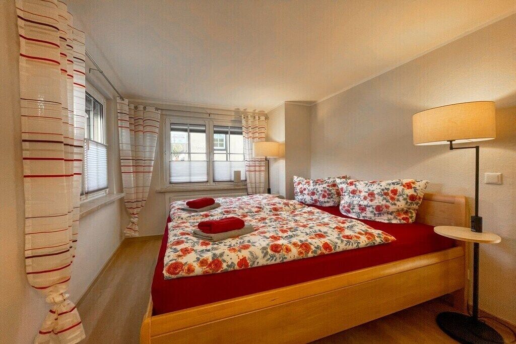 Een slaapkamer met een bed, gordijnen, een bedlampje en een raam.
