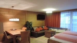Et hotelværelse med væg i træ, fjernsyn ophængt over en sofa, et spisebord med stole og en seng med ternet sengetøj.