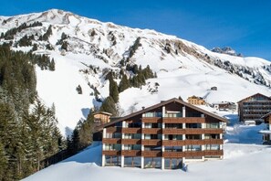 Ein mehrstöckiges Hotel im traditionellen Chalet-Stil, umgeben von schneebedeckten Bergen und Kiefern.