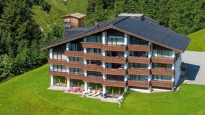 Et hotel med flere etager, altaner, en skilift og et bjerglandskab i baggrunden.