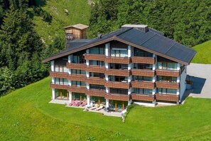 Un hotel a più piani con balconi, una seggiovia e montagne sullo sfondo.