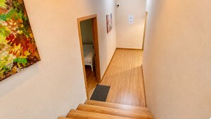 Un estrecho pasillo con suelo de madera que conduce a un dormitorio con cama y puerta.
