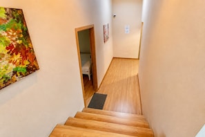 A narrow hallway with wooden flooring leading to a bedroom with a bed and a door. - Wisdom Muangthong Hostel (Pak Kret)