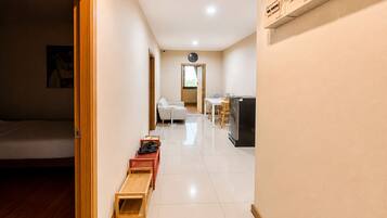 A hotel room with a bed, a wooden bench, a small table, a chair, and a kitchenette area.