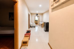 A hotel room with a bed, a wooden bench, a small table, a chair, and a kitchenette area.