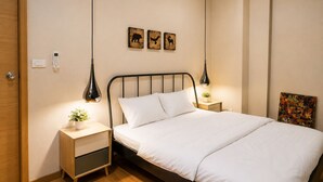 A neatly made bed with white linens, a bedside table with a lamp, and a wall-mounted phone. - Wisdom Muangthong Hostel (Pak Kret)