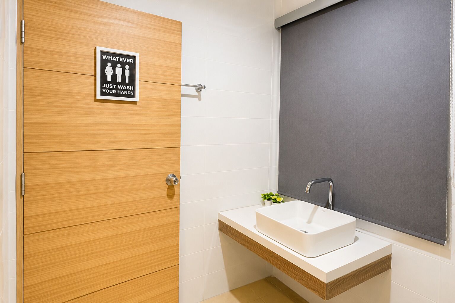 Ein Badezimmer mit Holztür, Waschbecken mit Spiegel und einem Schild, das zum Händewaschen auffordert.