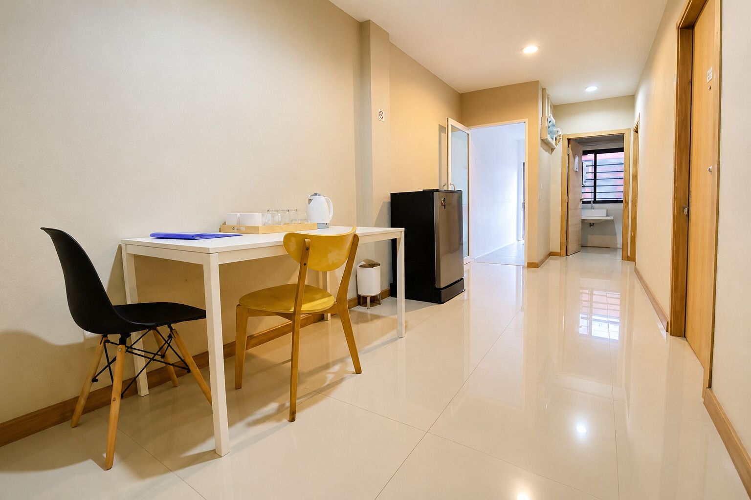 A clean, modern kitchen with a white countertop, a black refrigerator, and a wooden chair.