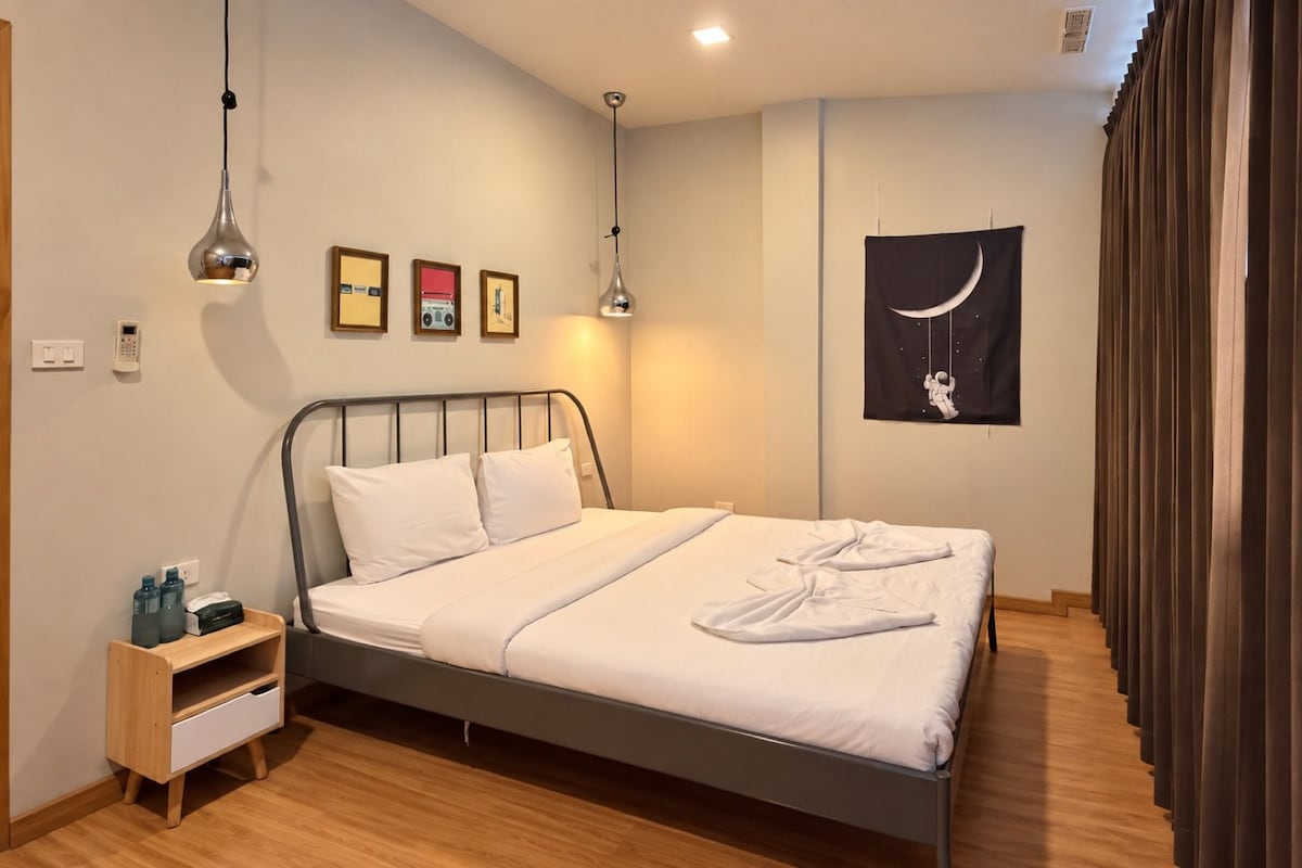 A neatly made bed with white linens, a bedside table with a lamp, and a wall with framed pictures.