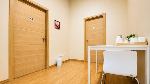 Habitación de hotel con dos puertas de madera, una silla blanca, una mesita con una bandeja y un cubo de basura.