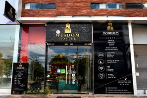 Moderni rakennus, jonka yläpuolella on kyltti, jossa lukee Wisdom Hostel. Kyltti kertoo, että majatalo tarjoaa yksinkertaisia, omilla wc- ja suihkutiloilla varustettuja huoneita sekä viihtyisän ympäristön.