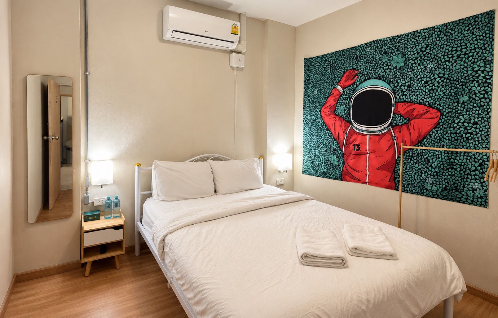 A hotel room with a bed, a nightstand, a mirror, an air conditioning unit, and a wall-mounted artwork.