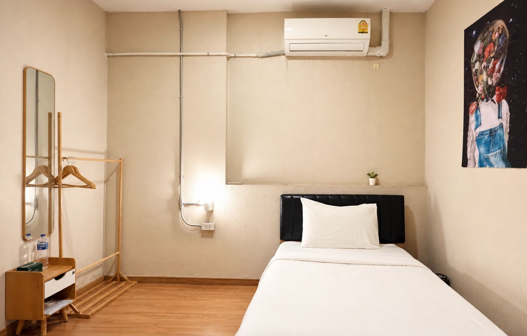 Quarto de hotel com cama, mesa de cabeceira, espelho, guarda-roupa, ar condicionado e uma obra de arte na parede.