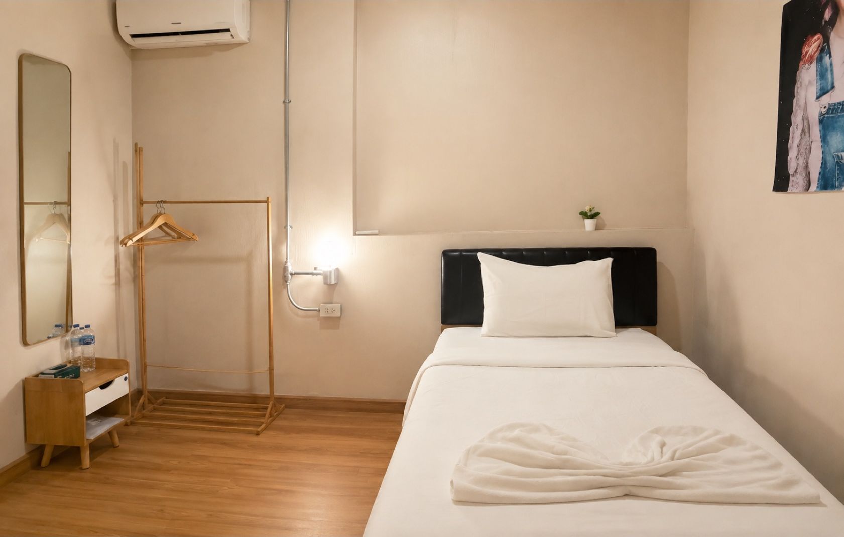 Habitación de hotel con cama, mesita de noche, espejo, perchero y una pequeña planta en maceta.
