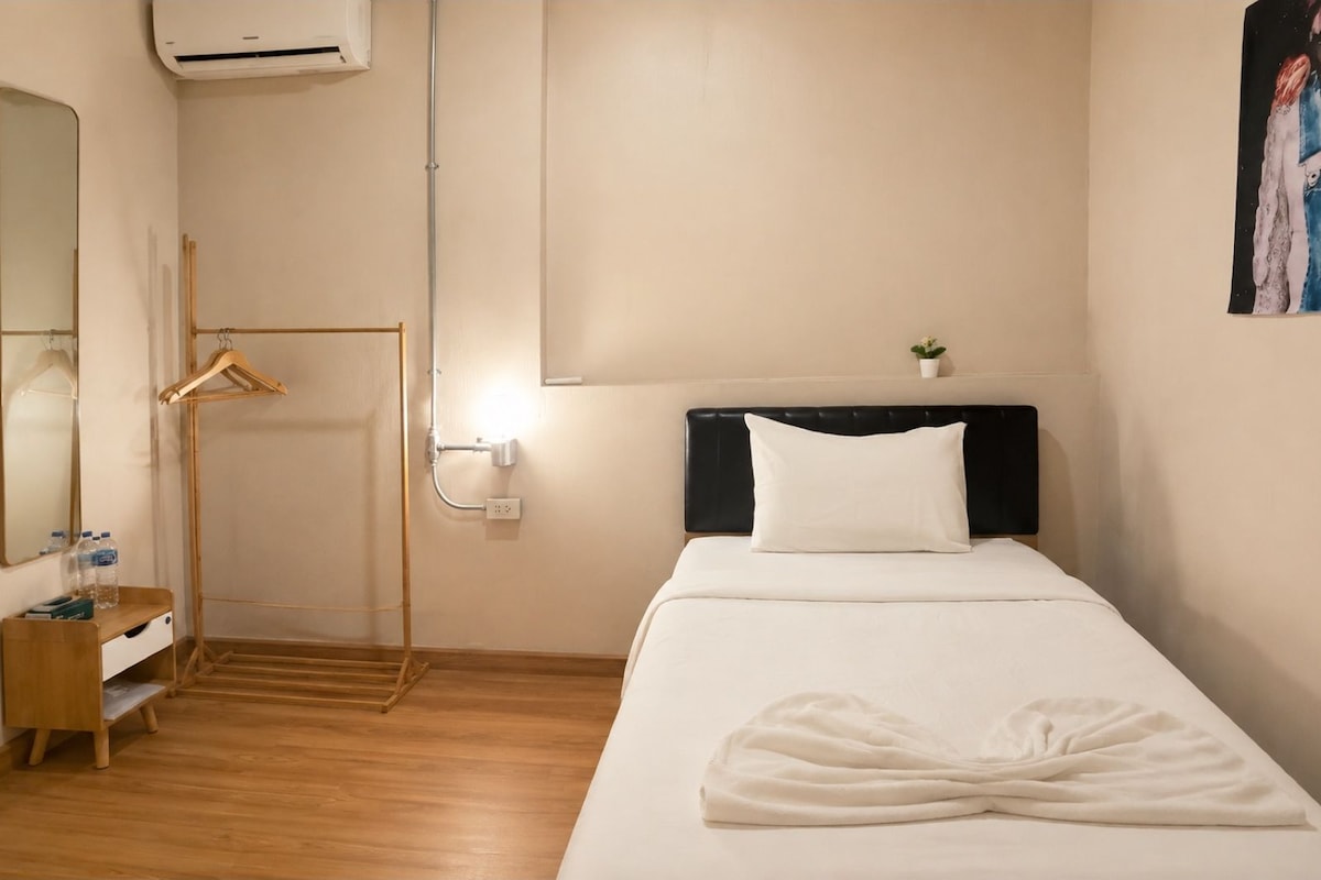 A hotel room with a bed, a bedside table, a mirror, a hanging clothes rack, and a small potted plant.