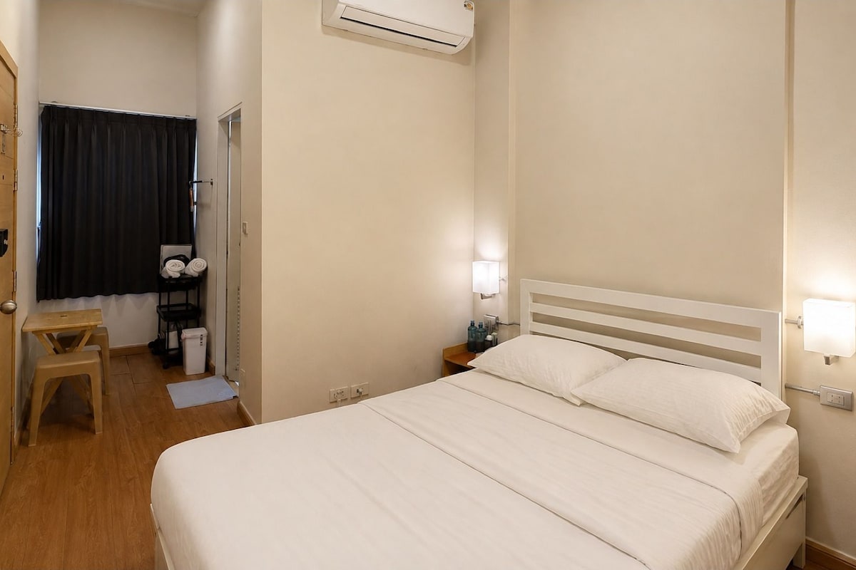 A hotel room with a bed, bedside table, lamp, and an air conditioning unit.