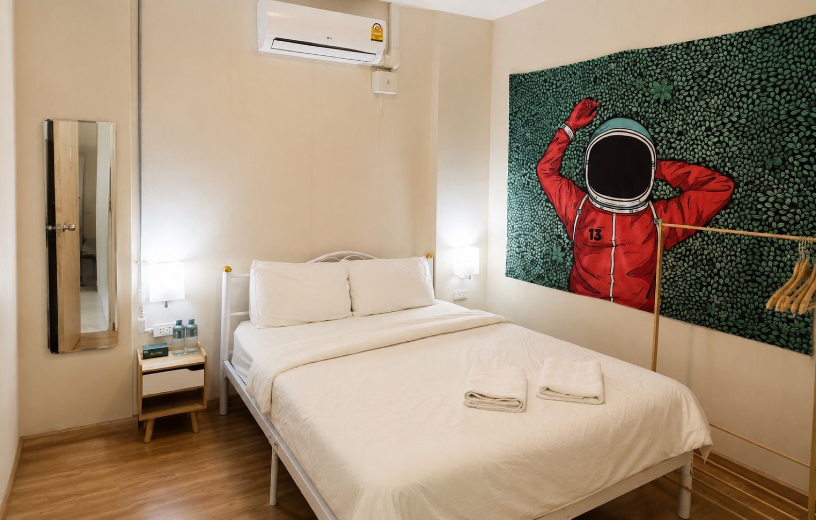 Habitación de hotel con cama, mesita de noche, espejo, unidad de aire acondicionado y una obra de arte colgada en la pared.