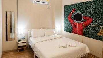Habitación de hotel con cama, mesita de noche, espejo, unidad de aire acondicionado y una obra de arte colgada en la pared.