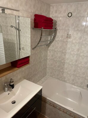 A bathroom with a white sink, a bathtub, and a towel rack with red towels. - Vrbo Property (Ehrwald)