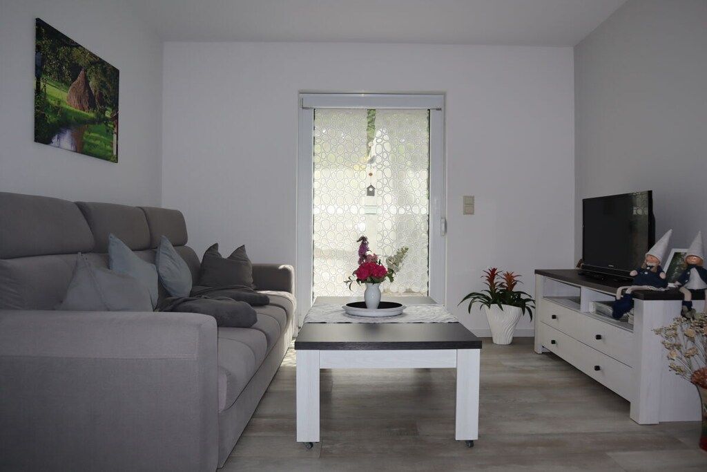 Una sala de estar moderna con un sofá, una mesa de centro, una televisión y una puerta corrediza de vidrio.