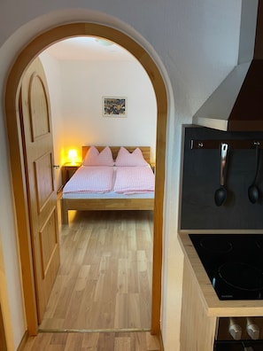 A bedroom with a bed, a wooden wardrobe, a wall-mounted TV, and a kitchen area with a stove. - Vrbo Property (Ehrwald)