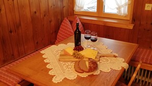 Puuinen ruokapöytä, jonka päällä on pitsinen pöytäliina, viinipullo, lasit ja juustolautanen.