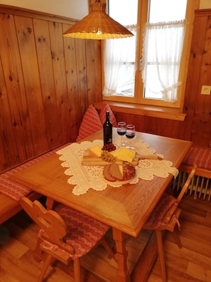 A wooden dining table with a lace tablecloth, a bottle of wine, glasses, and a cheese board. - Vrbo Property (Ehrwald)