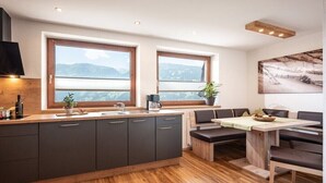 A modern kitchen with a central island, two windows with mountain views, and a dining area with benches. - Holiday apartment with 3 bedrooms (Zell am Ziller)