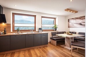 A modern kitchen with a central island, two windows with mountain views, and a dining area with benches. - Holiday apartment with 3 bedrooms (Zell am Ziller)