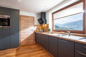 Une cuisine moderne avec un plancher en bois, des armoires grises, un four encastré et une fenêtre donnant sur les montagnes.