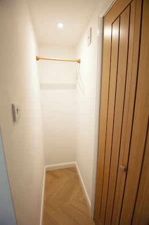 A narrow hallway with a wooden door on the right, a wooden floor, and a ceiling light.