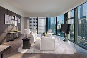 Quarto de hotel moderno com uma janela grande, televisão de tela plana, um conjunto de sofás, uma mesa de centro e uma mesinha de cabeceira.