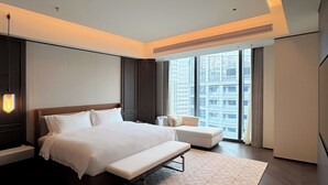 Ein modernes Hotelzimmer mit einem großen Bett, einer Bank, einer Sitzecke und Blick auf die Stadtlandschaft.