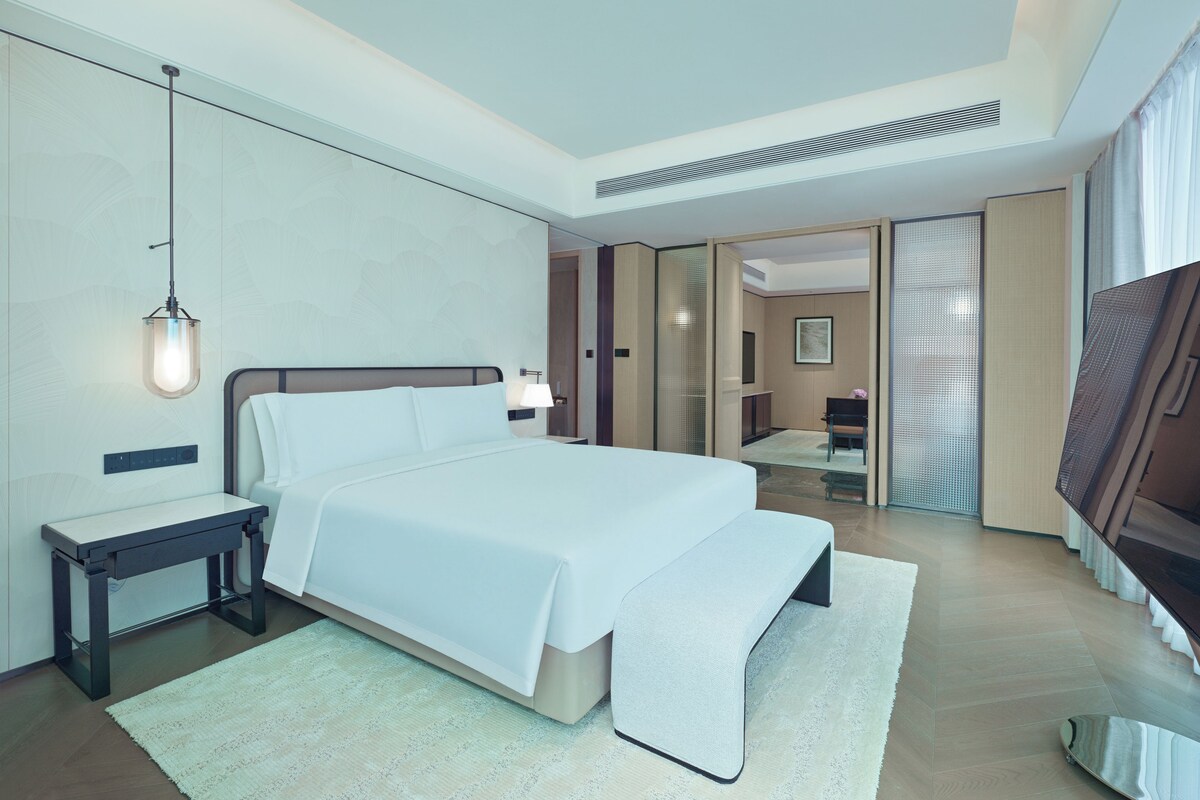 Quarto de hotel moderno com uma cama grande, mesas de cabeceira, escrivaninha e televisão.