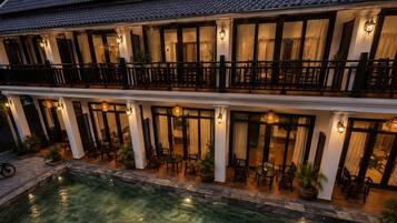 A two-story building with a swimming pool, outdoor seating, and a balcony.