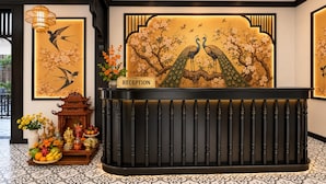 En receptionsdisk med et skilt der står 'RECEPTION', omgivet af traditionel indretning, herunder en vase med blomster, en skål med frugt og en dekorativ piedestal.