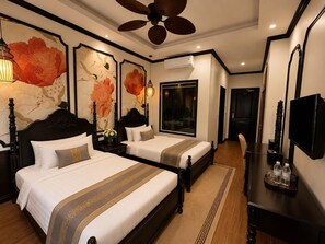 A hotel room with two beds, a ceiling fan, artwork on the walls, a TV, and a minibar. - Luang Prabang Indochine Heritage Hotel (Luang Prabang)